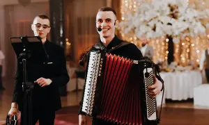 Dwóch muzyków przygotowuje się do biesiady. Jeden gra na akordeonie, drugi trzyma tamburyn.