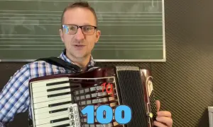 Mężczyzna gra na akordeonie, przygotowując się do lekcji piosenki na akordeon biesiadne. Na ekranie widnieje napis "100".