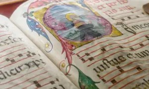 Stara księga z iluminacjami. Widać fragment rękopisu z nutami i ozdobnym inicjałem. Cała nuta jest tu częścią średniowiecznej notacji muzycznej.