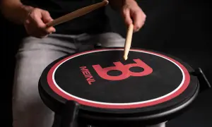 Ręce perkusisty ćwiczą na padzie perkusyjnym Meinl. Ciemne tło podkreśla czerwone logo.