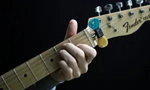 Dłoń grająca akordy na gryfie gitary Fender Telecaster. Kostki do gitary w uchwycie.