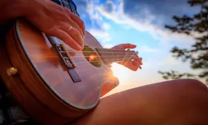 Dłoń grająca na ukulele na tle zachodzącego słońca.