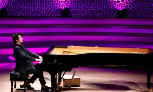 Pianista gra na czarnym fortepianie Steinway & Sons na scenie z fioletowym oświetleniem.
