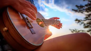 Dłoń grająca na ukulele na tle zachodzącego słońca.