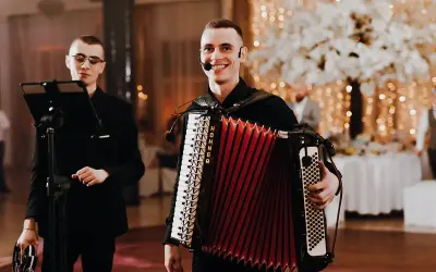 Dwóch muzyków przygotowuje się do biesiady. Jeden gra na akordeonie, drugi trzyma tamburyn.