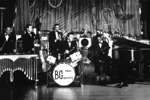 Zespół gra na instrumentach: wibrafonie, kontrabasie, perkusji z napisem BG Trio Sextette, gitarze i pianinie. To instrumenty Benny'ego Goodmana.