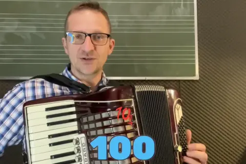 Mężczyzna gra na akordeonie, przygotowując się do lekcji piosenki na akordeon biesiadne. Na ekranie widnieje napis "100".