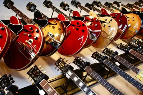 Rząd gitar elektrycznych w różnych kolorach i kształtach, od klasycznych po nowoczesne.