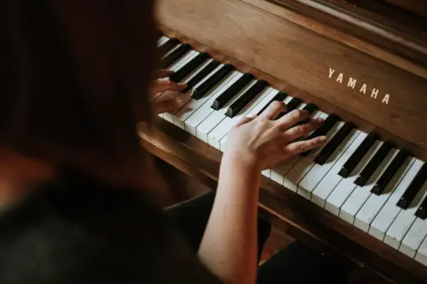 Dłonie na klawiaturze pianina Yamaha. Rozpoczyna się nauka gry na pianinie online, odkrywanie melodii.