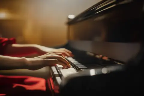Dłonie grające na klawiszach fortepianu w czerwonej sukience.