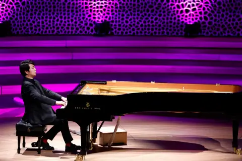 Pianista gra na czarnym fortepianie Steinway & Sons na scenie z fioletowym oświetleniem.
