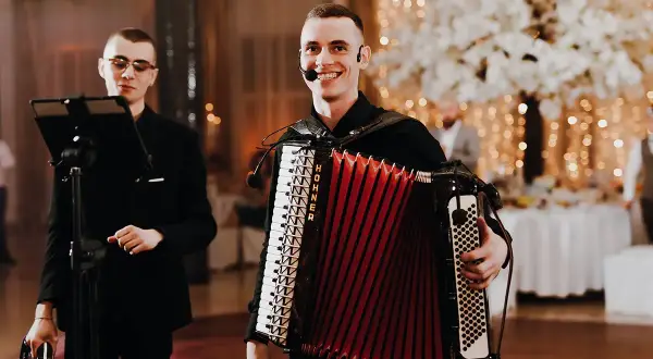 Dwóch muzyków przygotowuje się do biesiady. Jeden gra na akordeonie, drugi trzyma tamburyn.