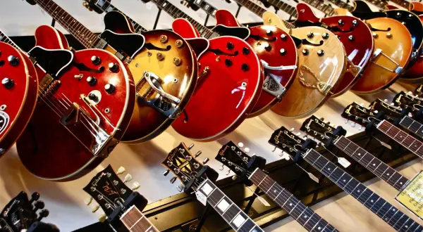 Rząd gitar elektrycznych w różnych kolorach i kształtach, od klasycznych po nowoczesne.