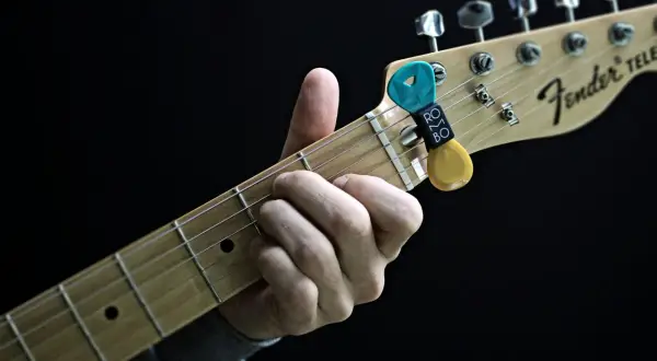 Dłoń grająca akordy na gryfie gitary Fender Telecaster. Kostki do gitary w uchwycie.
