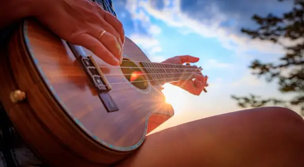 Dłoń grająca na ukulele na tle zachodzącego słońca.