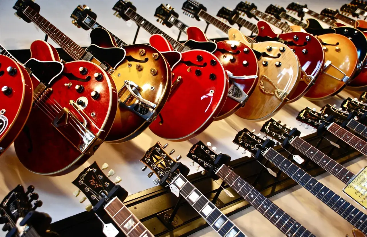 Rząd gitar elektrycznych w różnych kolorach i kształtach, od klasycznych po nowoczesne.