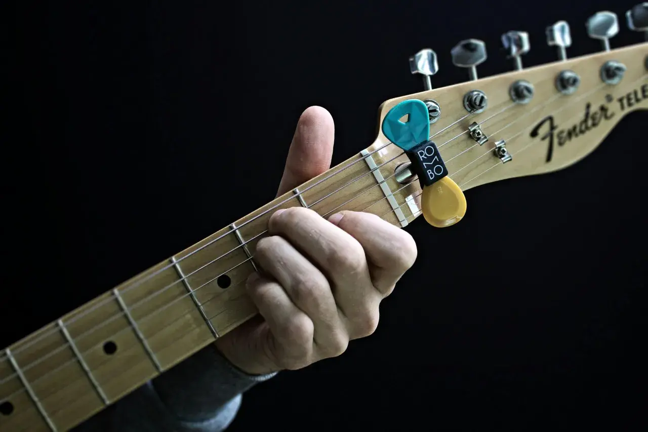 Dłoń grająca akordy na gryfie gitary Fender Telecaster. Kostki do gitary w uchwycie.