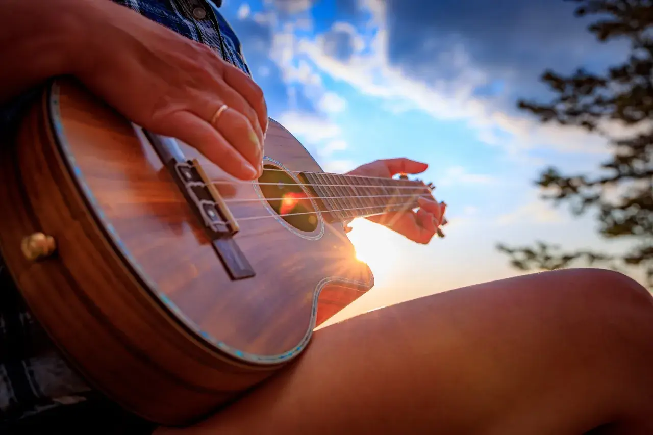 Dłoń grająca na ukulele na tle zachodzącego słońca.