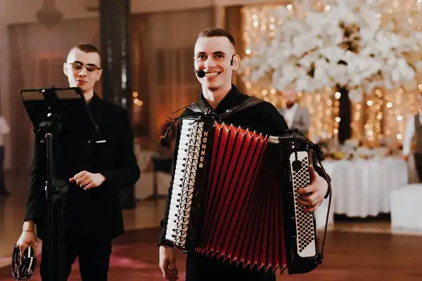 Dwóch muzyków przygotowuje się do biesiady. Jeden gra na akordeonie, drugi trzyma tamburyn.