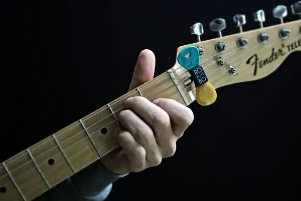 Dłoń grająca akordy na gryfie gitary Fender Telecaster. Kostki do gitary w uchwycie.